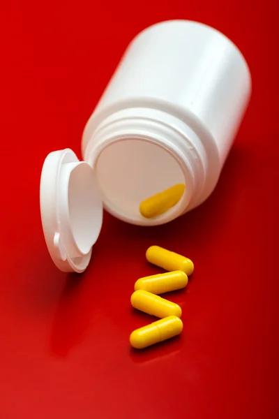 White tube of yellow pills isolated on red background — Stock Photo, Image