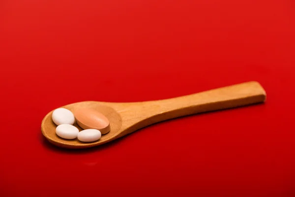 White pills on wooden spoon isolated on red background — Stock Photo, Image