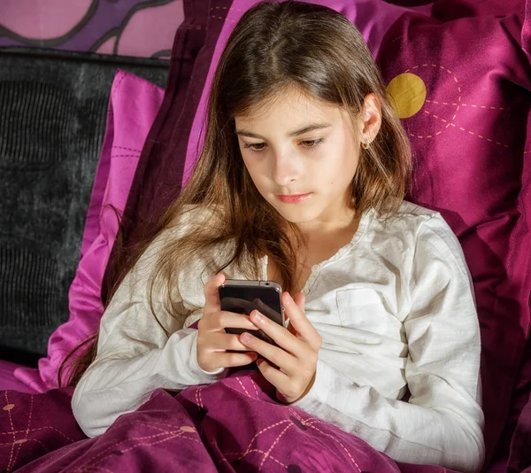 Beautiful young woman using cell phone in bed — Stock Photo, Image