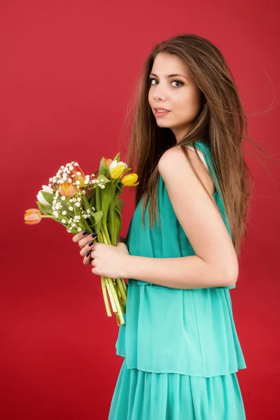 Mooi meisje in een zomer jurk met tulpen op een rode achtergrond — Stockfoto