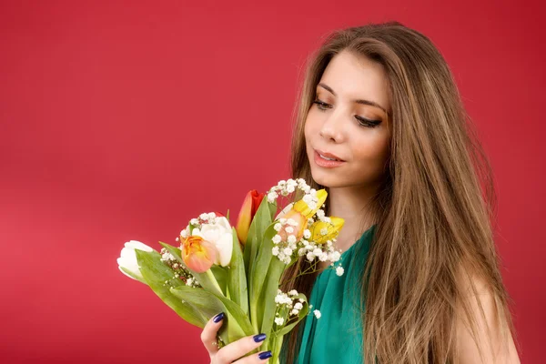 Schönes Mädchen in einem Sommerkleid mit Tulpen auf rotem Hintergrund — Stockfoto