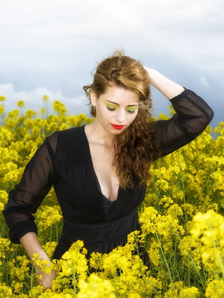 Krásná mladá žena v černých šatech ve žlutém poli — Stock fotografie