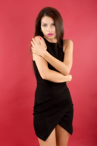 Sexy morena mujer en negro vestido aislado en rojo fondo —  Fotos de Stock