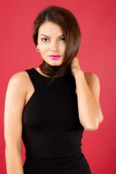 Sexy brunette vrouw in zwarte jurk geïsoleerd op rode achtergrond — Stockfoto