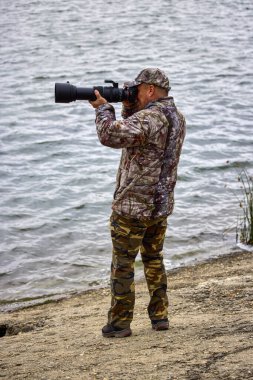 Kamuflaj giysileri içinde profesyonel fotoğrafçı doğada çalışıyor. sonbahar günü.