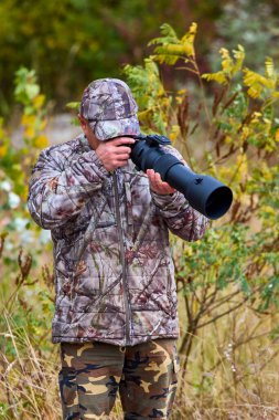 Kamuflaj giysileri içinde profesyonel fotoğrafçı doğada çalışıyor. sonbahar günü.