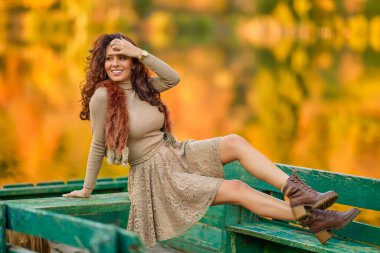 Güneşli bir sonbahar gününde gölün kenarında poz veren zarif bir kadın..