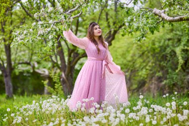 a young woman in a pink dress posing next to a blossoming apple, spring portrait.
