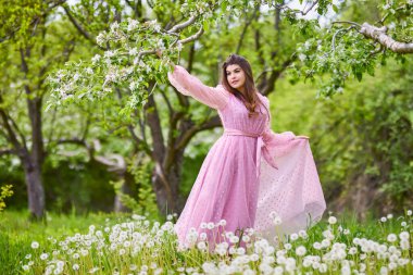 a young woman in a pink dress posing next to a blossoming apple, spring portrait.