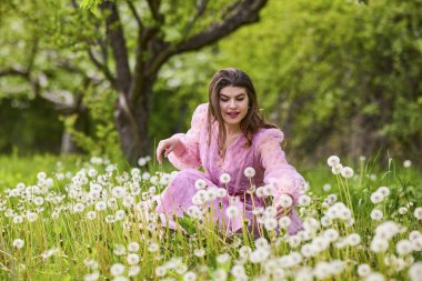 Pembe elbiseli genç bir kadın çiçek açan bir elmanın yanında poz veriyor, bahar portresi..