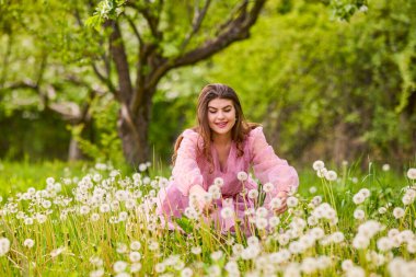 Pembe elbiseli genç bir kadın çiçek açan bir elmanın yanında poz veriyor, bahar portresi..