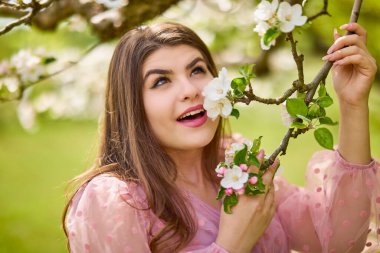 a young woman in a pink dress posing next to a blossoming apple, spring portrait.