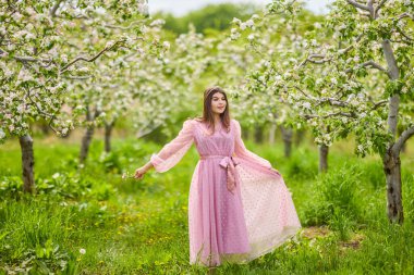 Pembe elbiseli genç bir kadın çiçek açan bir elmanın yanında poz veriyor, bahar portresi..
