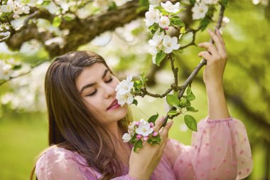 a young woman in a pink dress posing next to a blossoming apple, spring portrait.