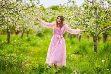 a young woman in a pink dress posing next to a blossoming apple, spring portrait.