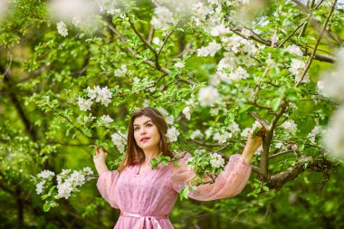 a young woman in a pink dress posing next to a blossoming apple, spring portrait.