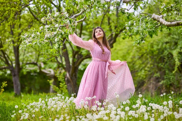 a young woman in a pink dress posing next to a blossoming apple, spring portrait.