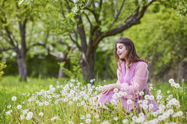 Pembe elbiseli genç bir kadın çiçek açan bir elmanın yanında poz veriyor, bahar portresi..