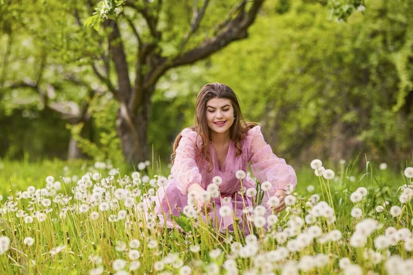 Pembe elbiseli genç bir kadın çiçek açan bir elmanın yanında poz veriyor, bahar portresi..