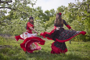 two dancers in traditional gypsy dresses dance in nature on a spring day
