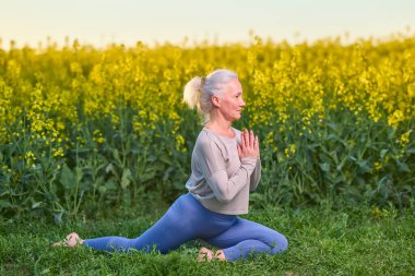 Yoga egzersizi, sabah rutini, gün batımı ışığı ve açık havada yeşil çimlerde dinlenen yaşlı bir kadın. Spor giyim sektöründe olgun bir kadın açık havada esneme hareketleri yapıyor. Yaş, sağlıklı yaşam tarzı.