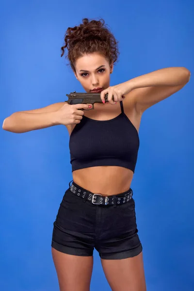 青い背景に銃を持った巻き毛の美しい若い女性 — ストック写真