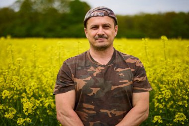 Çiçekli bir tarlada kamuflaj giysileri içinde çiftçi.