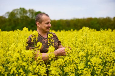 Çiçekli bir tarlada kamuflaj giysileri içinde çiftçi.