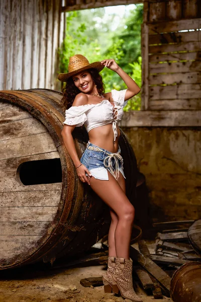 Woman in straw cowboy hat near old wooden barrel on brown wooden wall background.