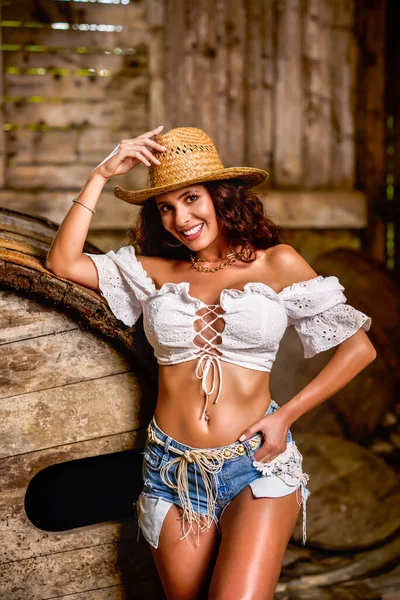 Woman in straw cowboy hat near old wooden barrel on brown wooden wall background.