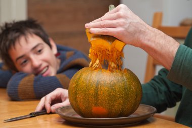 Baba ve oğul mutfak masasının üzerinde halloween kabak oyma