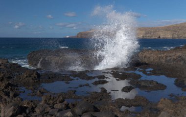 Gran Canaria, kuzey batı kıyısı doğal yüzme havuzları etrafında Salinas de Agaete, eski aşınmış karanlık lav platformuna karşı dalgalar kırılıyor.