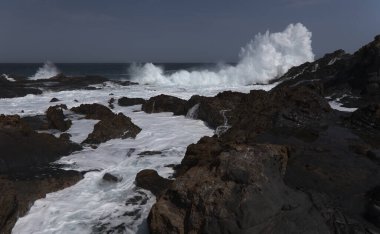 Gran Canaria, kuzey kıyısı, Puertillo de Banaderos çevresindeki kayalıklar okyanus dalgalarından korunan volkanik kaya bariyerleriyle korunuyor.
