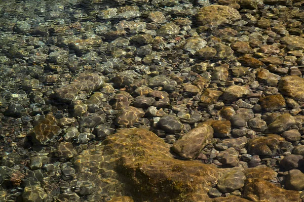 小石で満たされた大きな岩のプールでの波紋と太陽の反射 — ストック写真