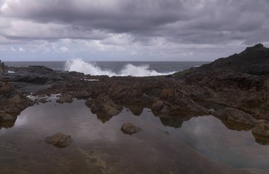 Gran Canaria, kuzey kıyısı, Puertillo de Banaderos çevresindeki kayalıklar okyanus dalgalarından korunan volkanik kaya bariyerleriyle korunuyor.