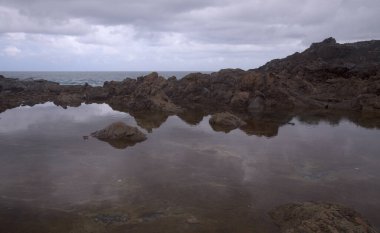 Gran Canaria, kuzey kıyısı, Puertillo de Banaderos çevresindeki kayalıklar okyanus dalgalarından korunan volkanik kaya bariyerleriyle korunuyor.