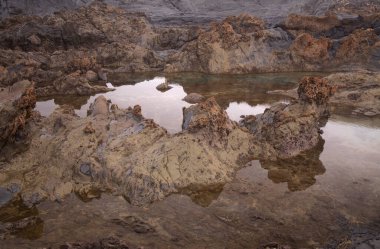 Gran Canaria, kuzey kıyısı, Puertillo de Banaderos çevresindeki kayalıklar okyanus dalgalarından korunan volkanik kaya bariyerleriyle korunuyor.