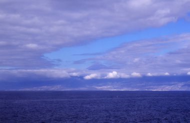 Tenerife, okyanus seviyesinden görüldüğü gibi, Teide zirvesi kısmen bulutlarla kaplı, Izana gözlemevinin beyaz yapıları sağda görünüyor.
