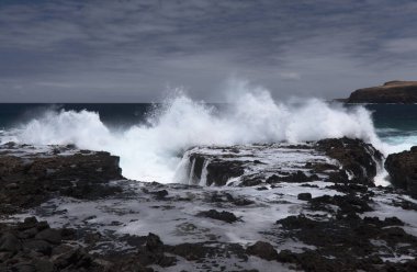 Gran Canaria, kuzey batı kıyısı doğal yüzme havuzları etrafında Salinas de Agaete, eski aşınmış karanlık lav platformuna karşı dalgalar kırılıyor.