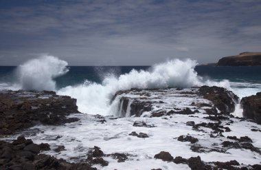 Gran Canaria, kuzey batı kıyısı doğal yüzme havuzları etrafında Salinas de Agaete, eski aşınmış karanlık lav platformuna karşı dalgalar kırılıyor.