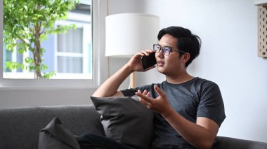 Genç adam koltukta dinleniyor ve cep telefonuyla konuşuyor..