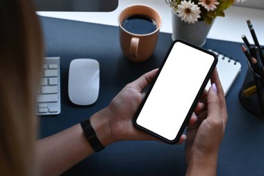 Genç bir kadın iş yerinde oturuyor ve akıllı telefon kullanıyor..