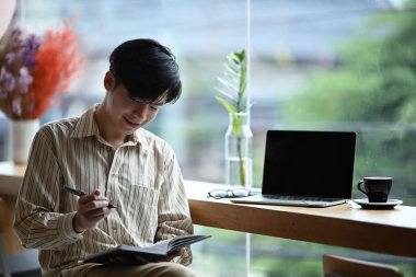 Gülümseyen genç adam parlak ofisinde oturuyor ve not alıyor..