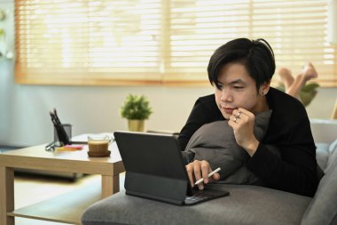 Kanepede uzanmış bilgisayar tabletiyle internette sörf yapan sıradan bir Asyalı..