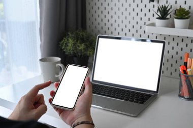 Kırpılmış genç adam ofiste oturuyor ve akıllı telefon kullanıyor..