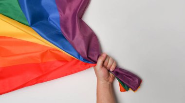 Beyaz arka planda LGBT gurur bayrağı tutan adam.