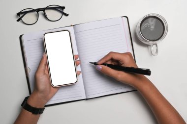 Yukarıda akıllı telefon tutan ve deftere yazan kadın var..