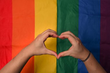 Erkek homoseksüel çift lgbt gökkuşağı arka planında el kalp işareti yapıyor.