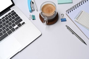 Dizüstü bilgisayarı, defteri ve kahve fincanı olan beyaz ofis masası..