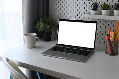 Laptop, ev bitkisi, kahve fincanı ve kalem tutacağı olan ofis masası..